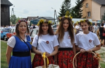 cztery kobiety, jedna w niebieskie sukni, trzy w bialych bluzkach i czerwonych ludowych spodnicach maja wianki na glowach, trzymaja kosze z przypinkami trzymaja kosze 