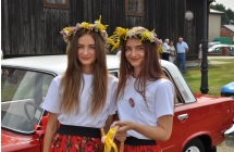 Dwie dziewczyny w bialych bluzkach maja wianki na glowach, w rece trzymaja kosz z przypinkami 