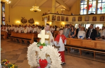 Na pierwszym planie wieniec dozynkowy, w tle kosciol z wiernymi