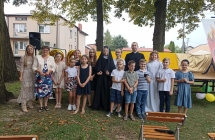 Grupa dzieci oraz ksiadz i kobieta pozuja przed scena