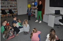 Siedzace przedszkolaki oraz kobieta i dziewczynka z balonami