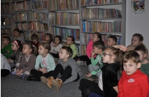 Grupa dzieci siedzi na dywanie na tle regalu z ksiazkami