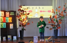 Dziewczynka w zielonej flanelowej koszuli na scenie, w tle napis lyzka