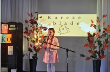 Dziewcvzynka w rozowej sukience na scenie, w tle napis kurcze blade
