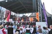 Zespół folklorystyczny na scenie. Pod sceną licznie zebrana publiczność w strojach ludowych 