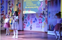 Dziewczynka śpiewająca na scenie, obok niej dwie tancerki 