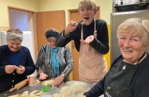 Trzy uśmiechnięte kobiety lepiące pierogi i młody mężczyzna trzymający łyżkę 
