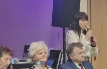 Kobieta mówiąca do mikrofonu, obok siedzą zaproszeni goście 