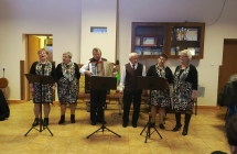 Zespół ludowy. Kilka kobiet i mężczyzna śpiewają oraz mężczyzna grający na akordeonie. 