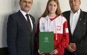 dwoch mezczyzn w garniturze oraz dziewczyna w bialo czerwonej bluzie sportowej z zielona teczka 