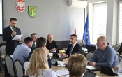 grupa ludzi siedząca przy stole, jedna osoba stoi i mówi przez mikrofon