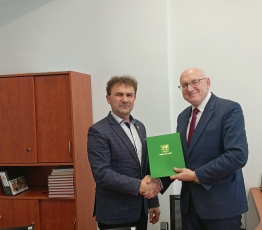 dwoch mezczyzn podaja sobie rece i trzymaja zielona teczke