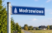 Znak z nazwa ulicy modrzewiowa. Bialy napis na niebieskim tle. w oddali wiejski krajobraz